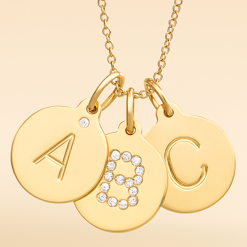 Gold necklace with three round pendants featuring letters 'A', 'B', and 'C' on a beige background.