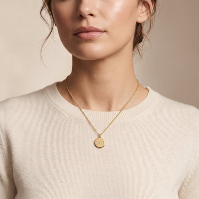 A close-up of a woman wearing a delicate gold chain necklace with a round gold pendant engraved with 11 11