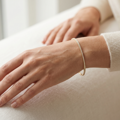 Close-up of a hand wearing a gold bracelet on a light background