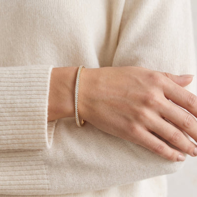 Hand wearing a gold bracelet on a light background
