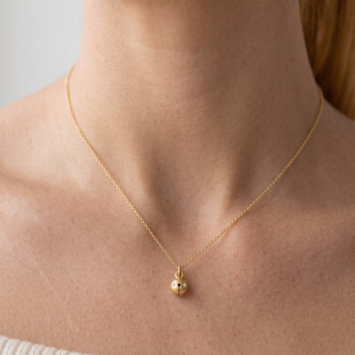 A close-up of a woman wearing a delicate gold chain necklace with a small, bell gold pendant.