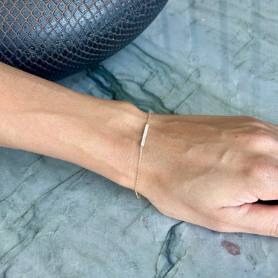 A delicate gold chain bracelet with a small white stone cluster, worn on a person's wrist resting on a gray marble surface.