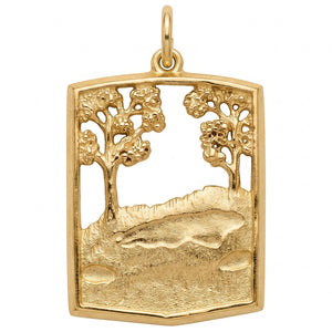 A gold pendant featuring an openwork landscape design with two stylized trees, a rocky hillside, and a fish motif in the center, shown on a plain white background.