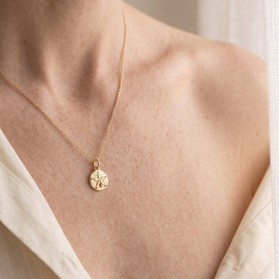 A close-up lifestyle shot of a model wearing a delicate gold chain necklace with a small circular starfish pendant, styled with a cream-colored blouse.