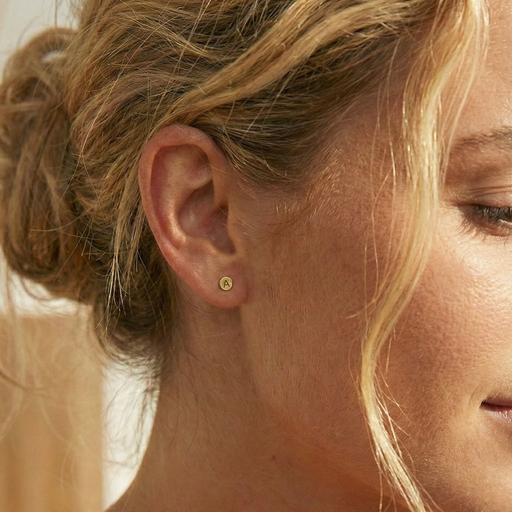 Close-up of a woman's ear wearing a gold earring with a blurred background