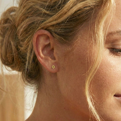 Close-up of a woman's ear wearing a gold earring with a blurred background