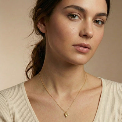 Woman wearing a gold necklace with a heart pendant against a beige background
